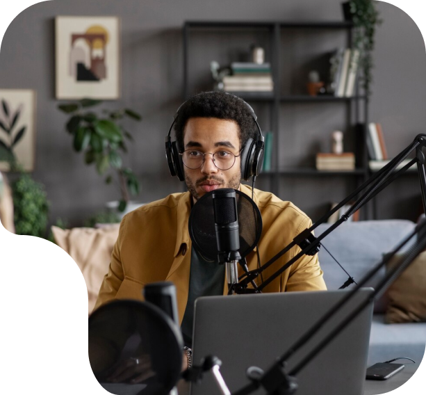 Man wearing headphones speaking into a microphone in a professional podcasting setup, with a laptop and modern decor in the background, illustrating podcast production services by PodcastCrew.