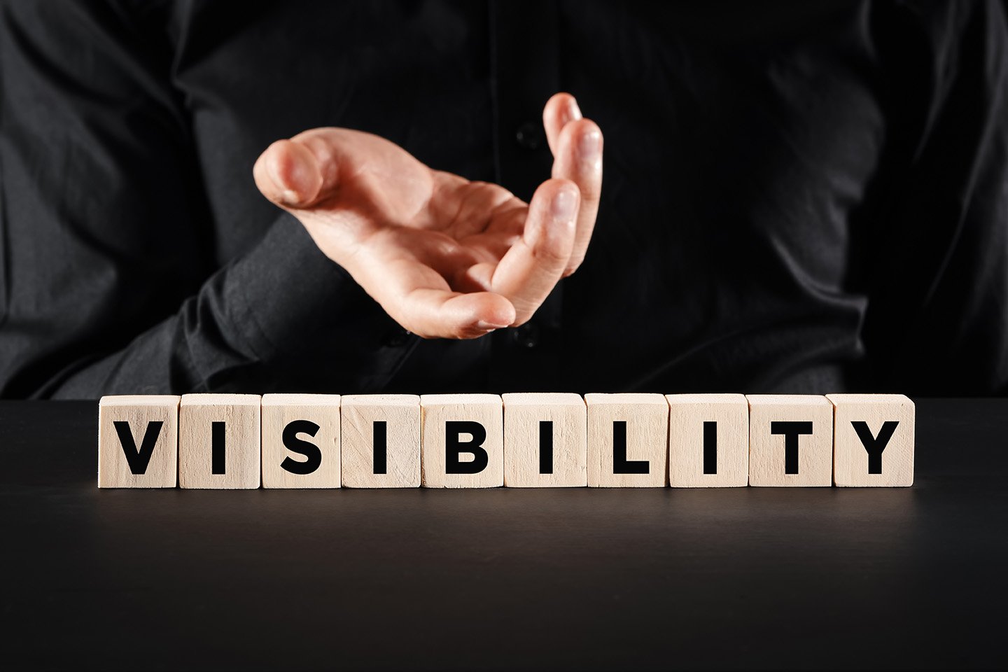 Hand gesturing towards wooden blocks spelling "VISIBILITY," emphasizing podcast discoverability and growth strategies.